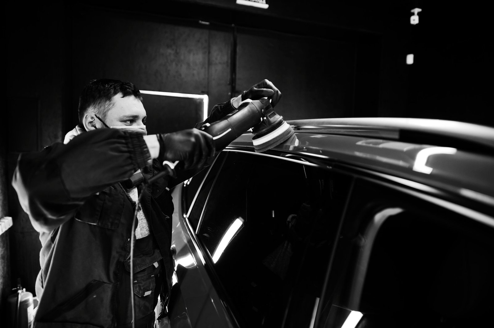 Car detailing concept. Man in face mask with orbital polisher in repair shop polishing orange suv car.